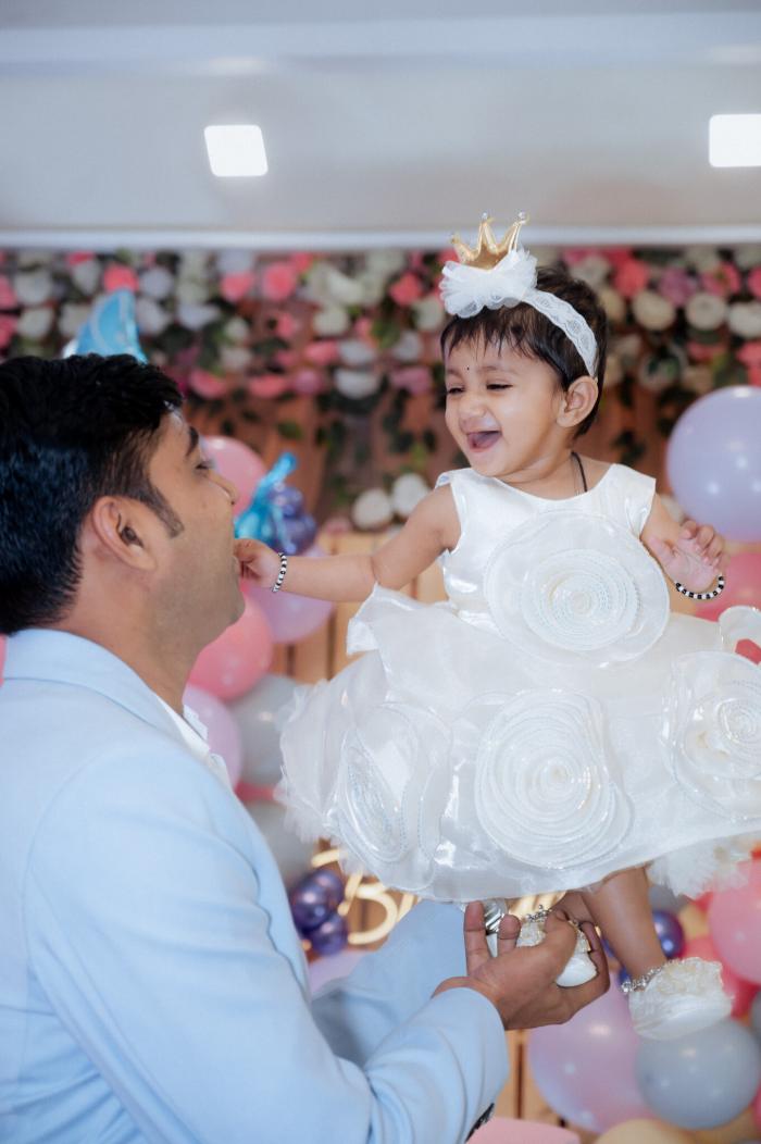 Father blowing bubbles for his baby daughter in a white dress at her birthday, by PickYouPic Prayagraj