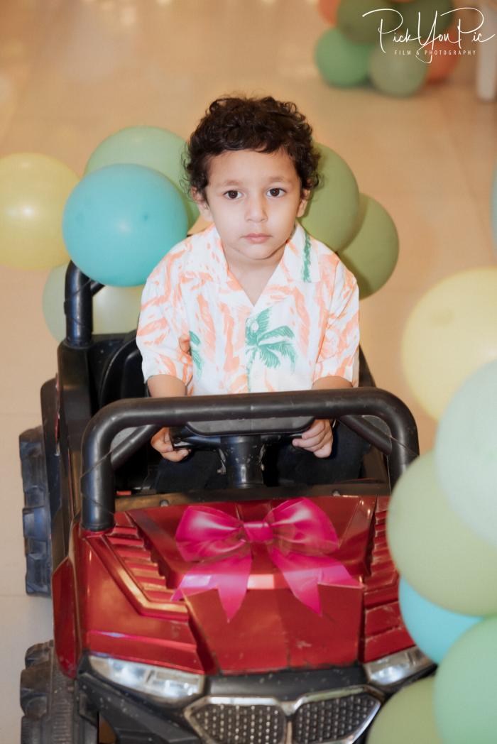 Toddler beside a gift with a pink bow and pastel balloons at his birthday party, by PickYouPic Prayagraj