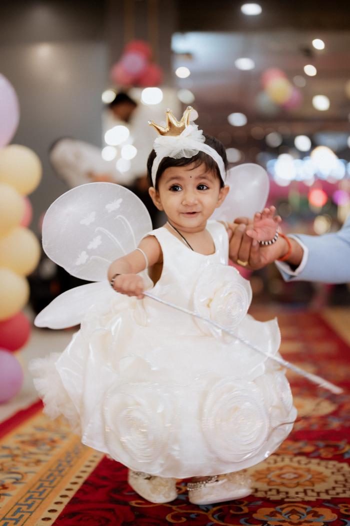 Baby girl in a white dress with a crown and fairy wand among balloons, birthday photography by PickYouPic Prayagraj