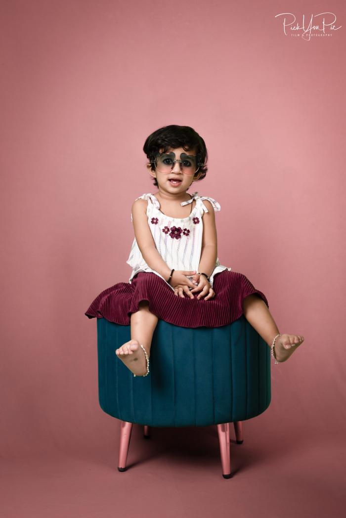 Kids studio portrait — girl in sunglasses seated on a teal stool against a pink backdrop, by PickYouPic Prayagraj