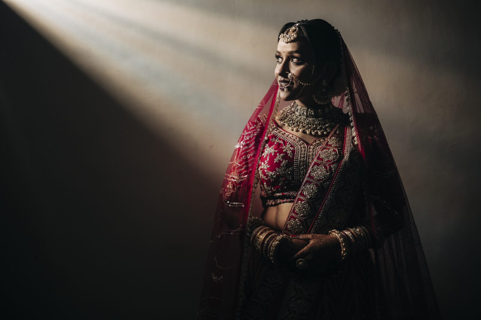Bride standing in a beam of light in her bridal lehenga, candid wedding photograph