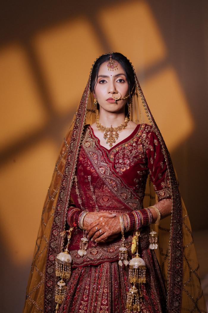 Bride in a maroon lehenga standing in patterned window light, Prayagraj