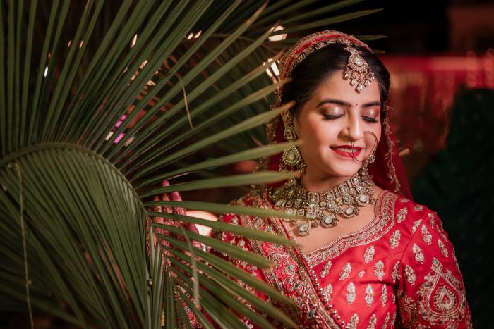 Bride framed by palm leaves in her red bridal lehenga, Prayagraj wedding