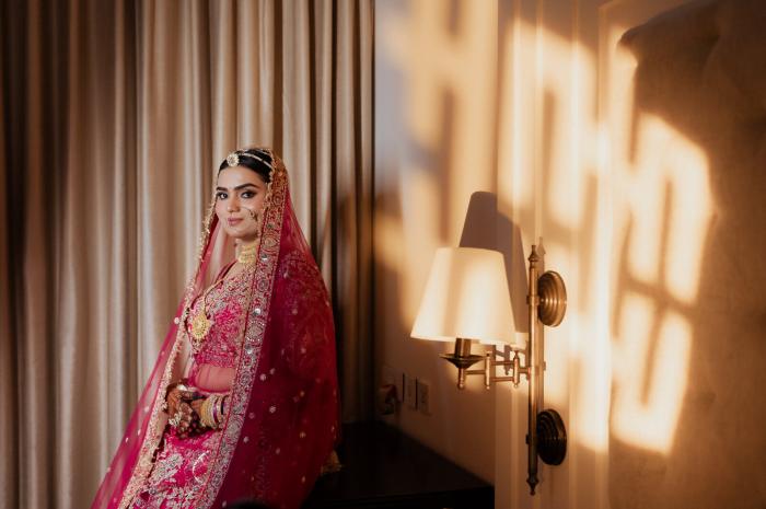 Bride in her red lehenga standing in patterned window light, Prayagraj wedding