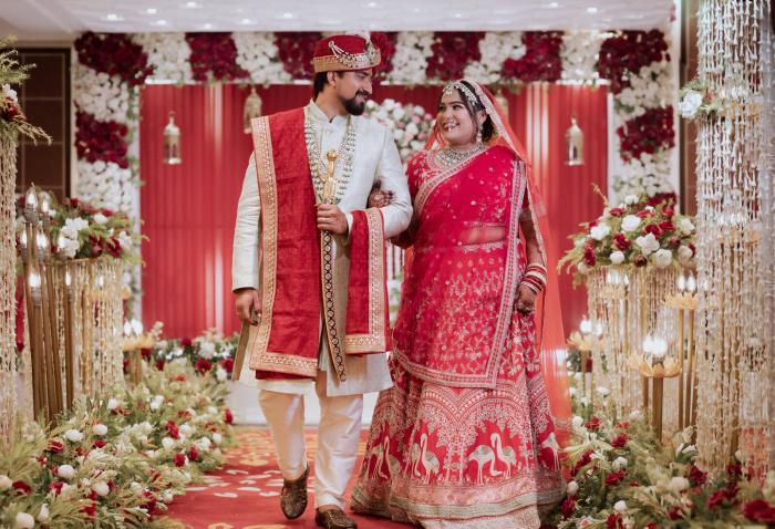 Bride and groom at the red floral wedding entrance, Prayagraj