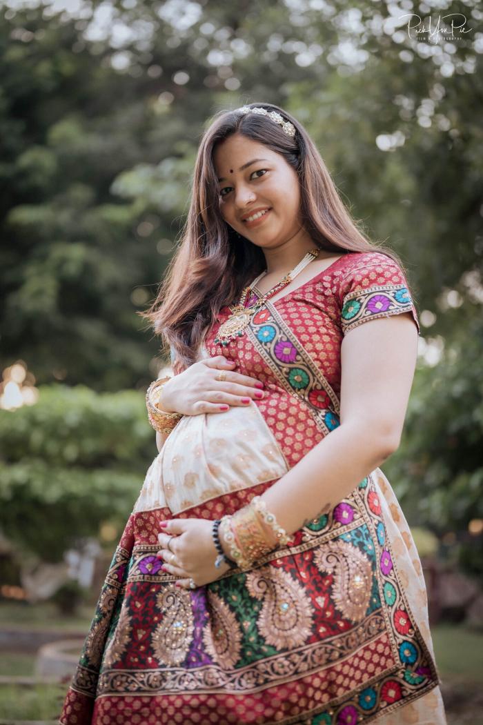 Expectant mother in an embroidered outfit standing outdoors among trees, maternity photoshoot by PickYouPic Prayagraj