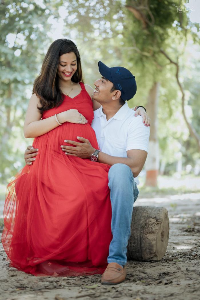 Expectant mother in a red gown with her husband outdoors, maternity photoshoot by PickYouPic Prayagraj