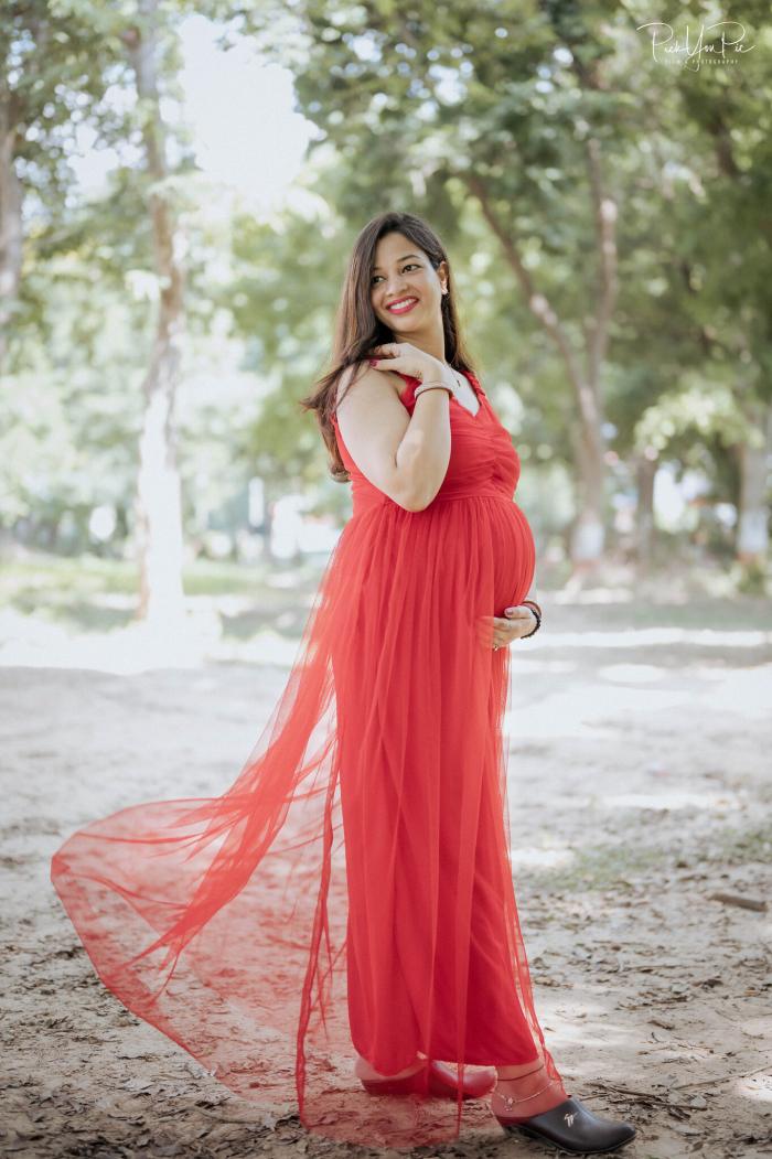 Mother-to-be in a flowing red gown with a long train in a park, maternity portrait by PickYouPic Prayagraj
