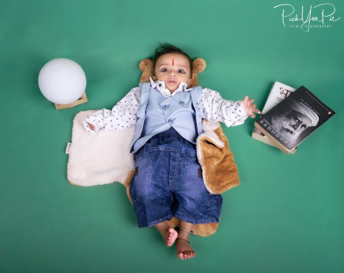 Newborn boy lying on a green backdrop dressed in a shirt and jeans with props around him, newborn photoshoot by PickYouPic Prayagraj
