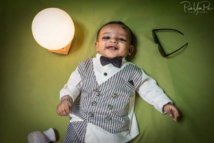 Baby boy in a checked waistcoat and bow tie lying on a green backdrop, newborn photoshoot by PickYouPic Prayagraj