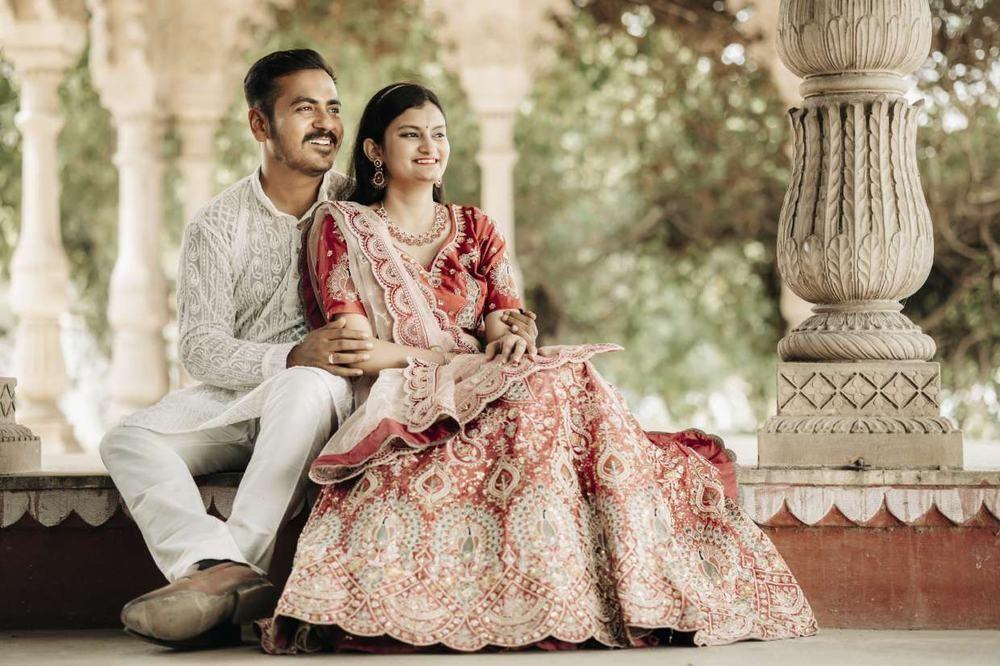 Couple seated on the marble steps of a pillared pavilion, bride-to-be in a pink lehenga