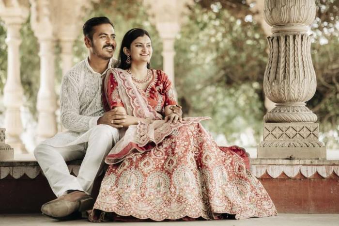 Couple seated on the marble steps of a pillared pavilion, bride-to-be in a pink lehenga