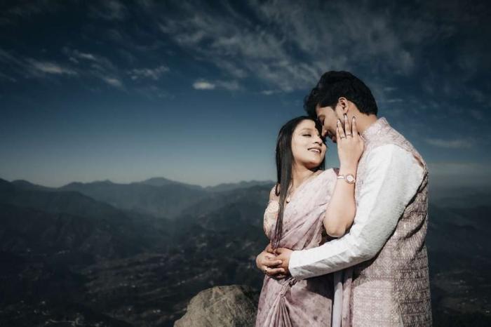 Couple embracing on a hilltop at dusk with a mountain valley behind them