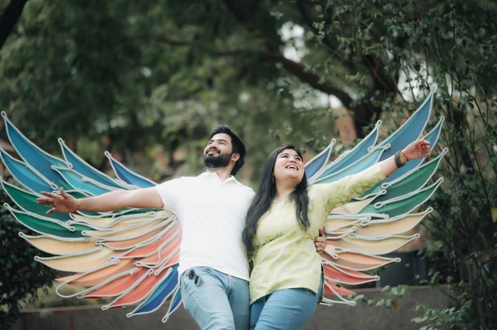 Couple standing with painted angel wings on a wall, arms spread wide