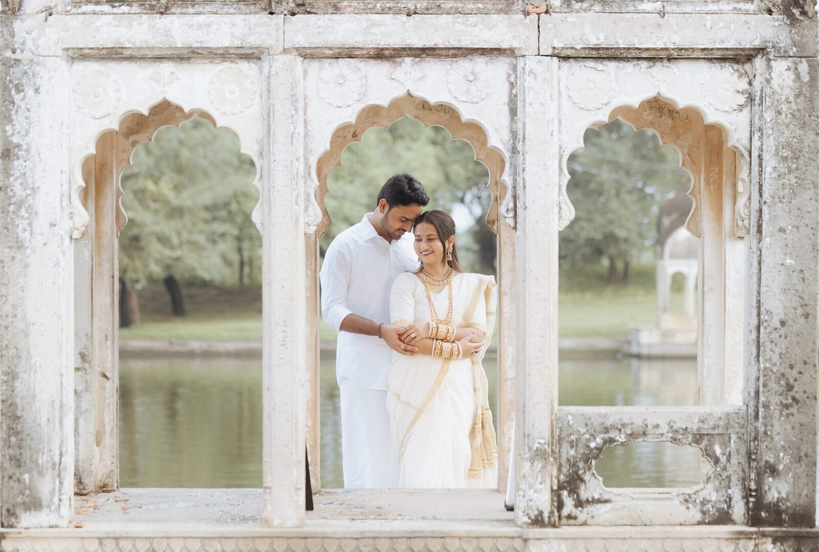 Couple framed in the weathered stone window of a lakeside pavilion, Ganesh Bagh Chitrakoot