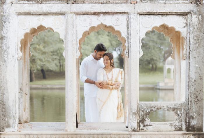 Couple framed in the weathered stone window of a lakeside pavilion, Ganesh Bagh Chitrakoot