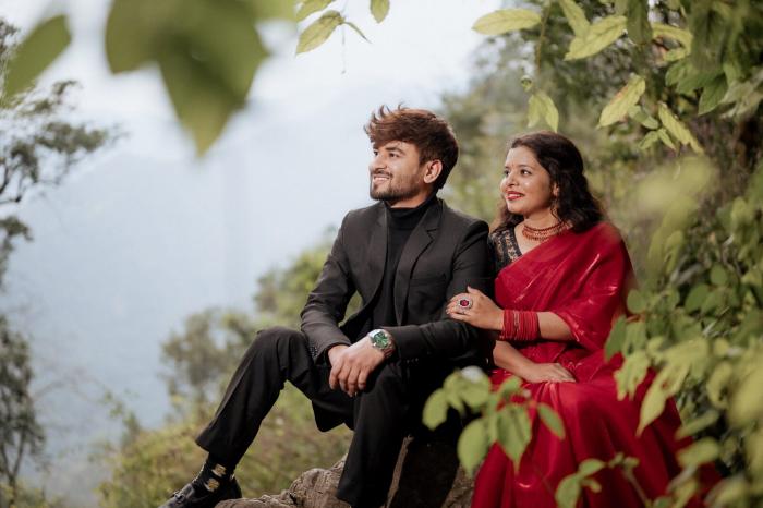 Couple sitting on a rock during a Nainital pre-wedding shoot with green hills behind