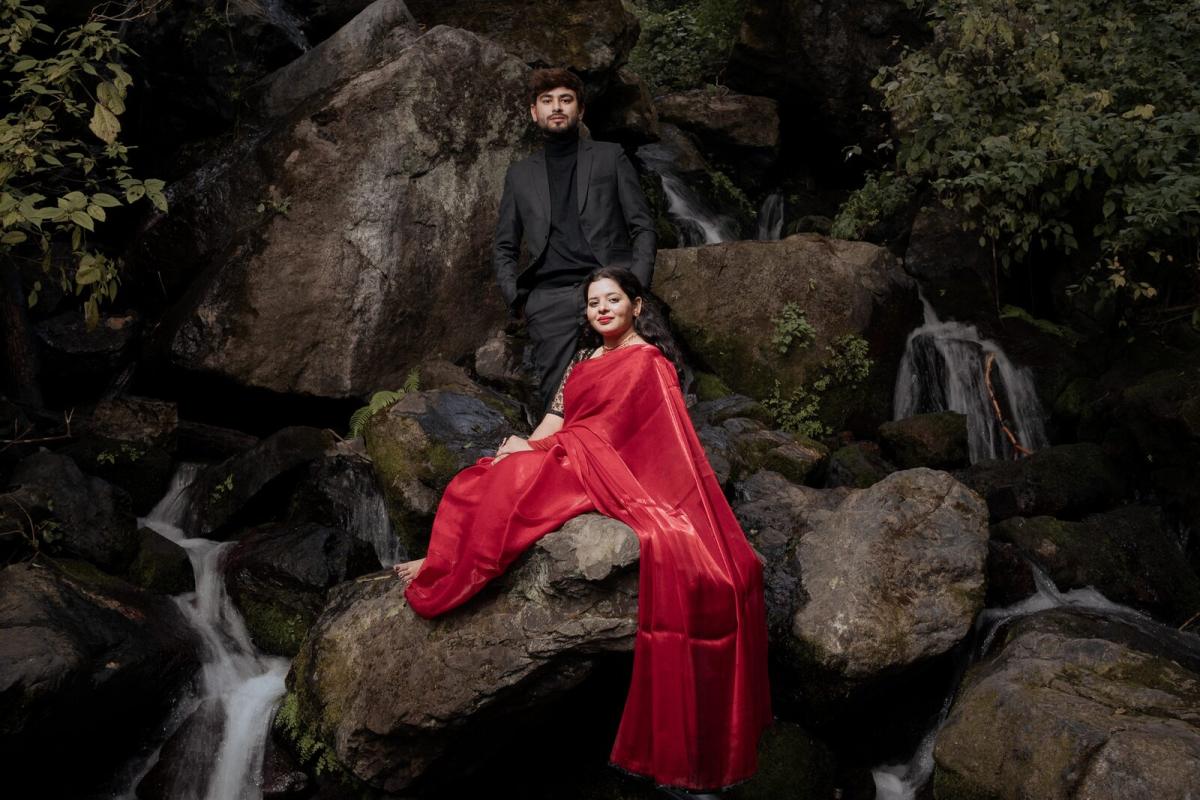 Red saree spread across mossy rocks beside a waterfall — Nainital pre-wedding shoot