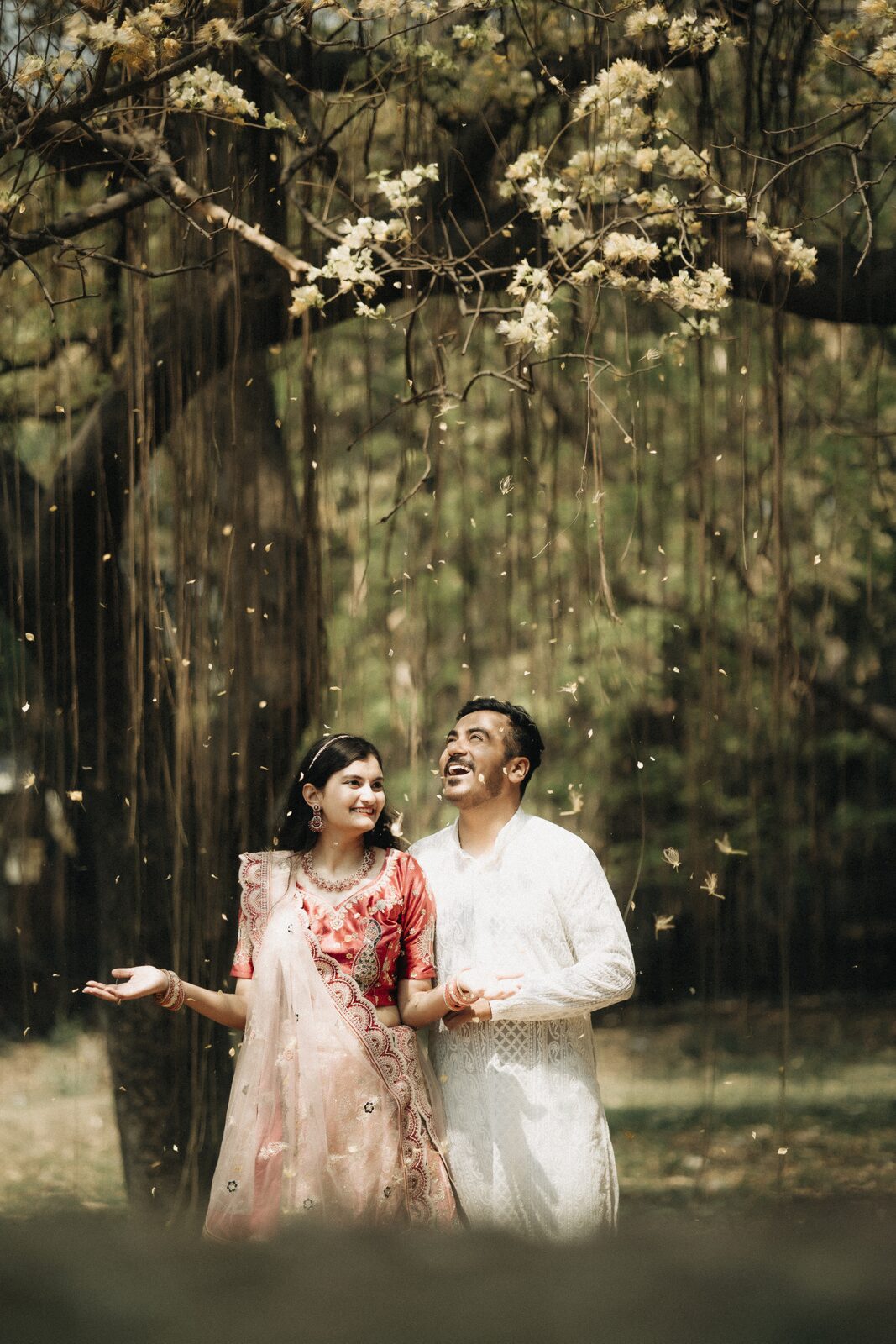 Couple laughing under a blossoming tree during their pre-wedding shoot