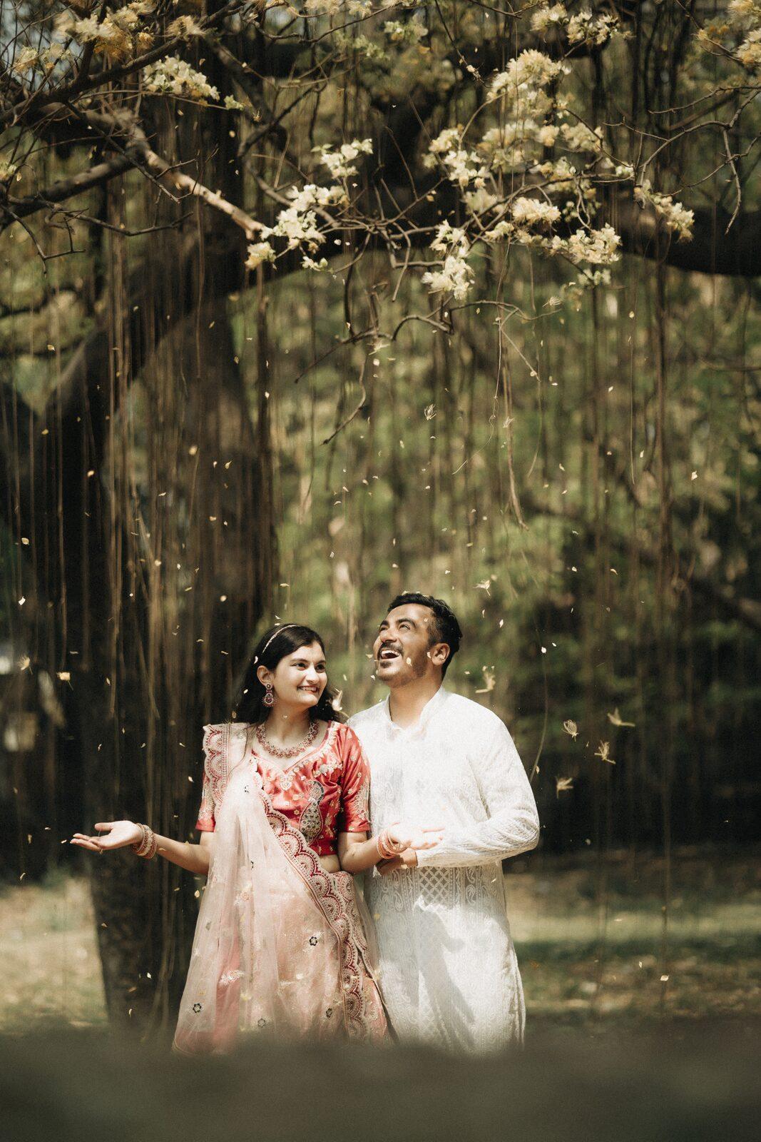 Couple laughing under a blossoming tree during their pre-wedding shoot