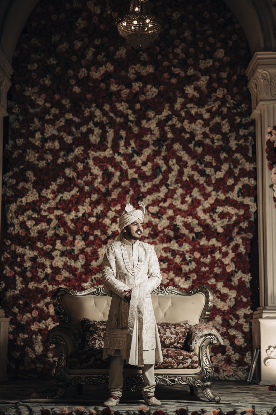Groom seated against a floral wall on the wedding stage, Prayagraj