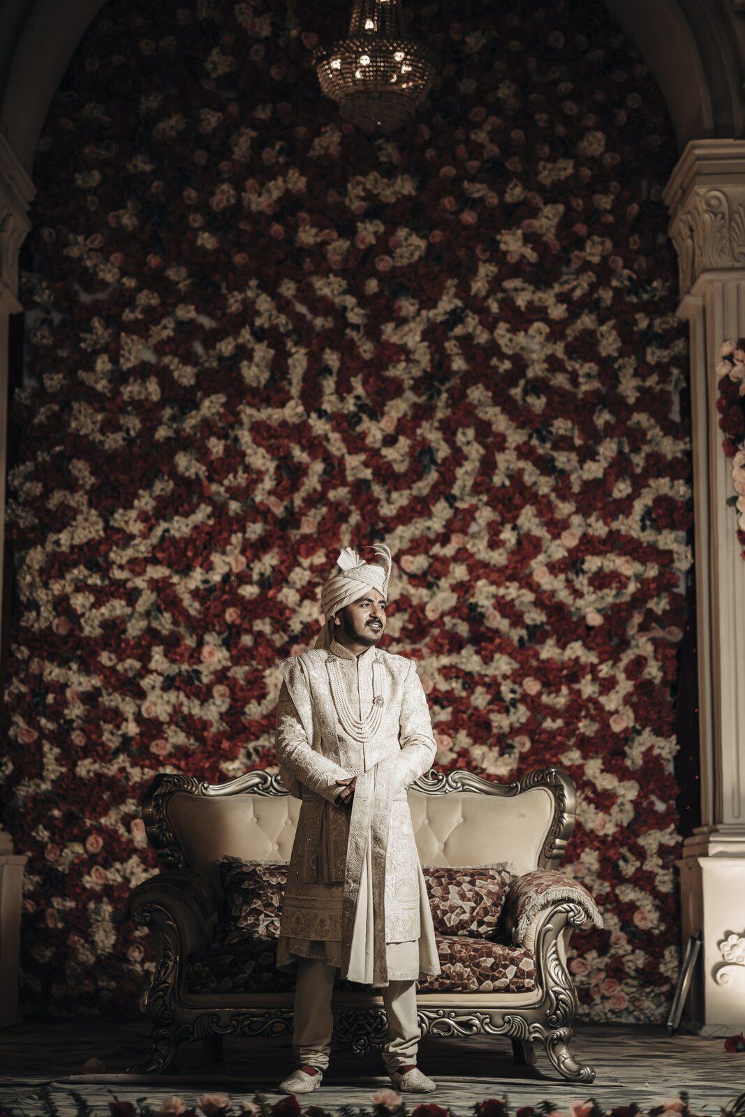 Groom seated against a floral wall on the wedding stage, Prayagraj